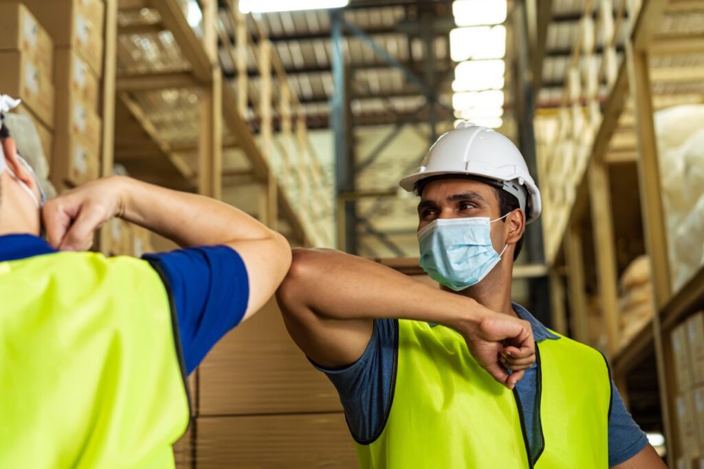masked warehouse workers bump elbows