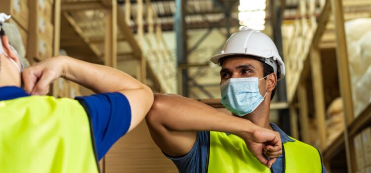 masked warehouse workers bump elbows