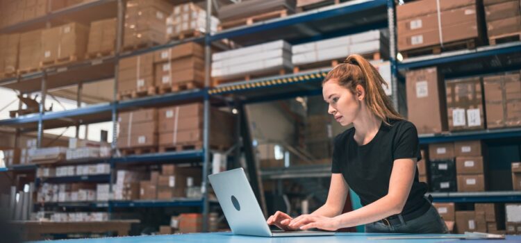 woman uses laptop in the middle of an ecommerce warehouse